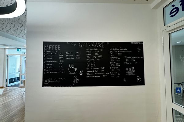 Auf dem Bild ist die Speisekarte (Tafel) im Innenraum des Cafés an einer Wand hängend zu sehen.