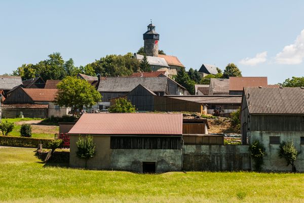 Vor einem Burgturm liegen die Häuser und Scheunen eines Dorfes.