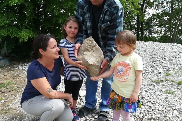 Vater, Mutter und zwei Kinder halten lächelnd einen großen Felsbrocken, in dem ein Fossil erkennbar ist.