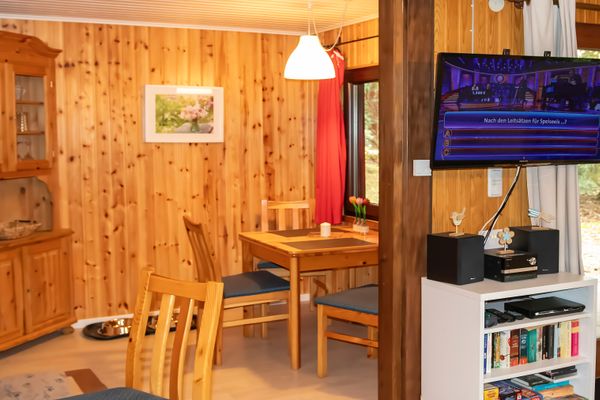 Essbereich mit Holztisch und Stühlen, Holzschrank und Fernseher an der Wand.