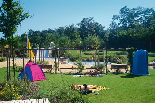 Liegewiese beim Freibad Bogen. Im Hintergrund der Kinderbereich mit verschiedenen Becken und breiter Wasserrutsche.