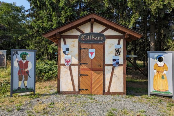 Das Bild zeigt das Zollhaus mit 2 Gemälden links und rechts. Dies befindet sich an der Schildwiese nahe Kleintettau.