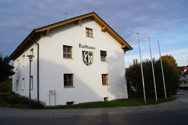 Rathaus in Neukirchen mit dem Ortswappen an der Hauswand. Auf den drei Masten vor dem Gebäude sind keine Fahnen gehisst.