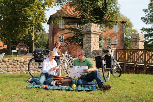 Familie macht vor der Burg Bodenteich ein Picknick auf einer Decke; daneben stehen zwei Fahrräder.