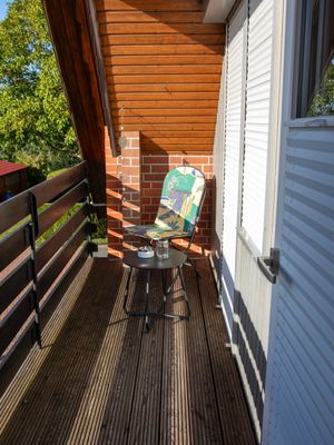 Schmaler Balkon mit Holzboden, Stuhl und kleinem Tisch neben einer Tür und Geländer.