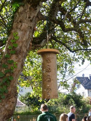 Insektenhotel hängt an einem Baum. Im Hintergrund Besucher die den Garten betrachten.