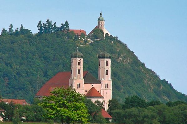 Dicht eingebettet in Bäume und Sträucher steht die Klosterkirche Oberalteich mit ihren markanten Doppeltürmen. Darüber steht majestätisch die Wallfahrtskirche Bogenberg.