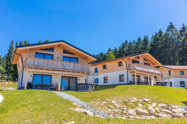 Feriendorf mit Chalets, große Balkone aus Holz, Terrasse mit Hotpot, im Hintergrund ein dichter Wald mit Nadelbäumen