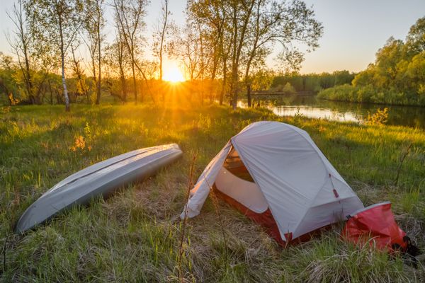Landscape with camping tent and kayak on the river at sunrise