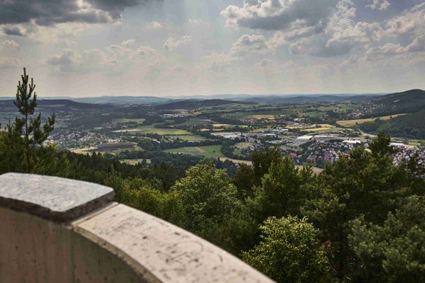 Das Bild zeigt Landschaft mit Wald und einer Stadt in der Entfernung. Es ist ein Panoramablick von einem Turm aus.
