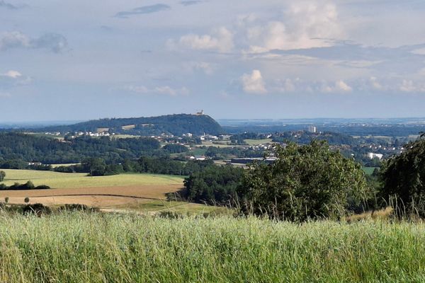 Im Vordergrund hohes Gras, dahinter einige Ortschafen zwischen Wiesen und Waldstücken, darüber thront die Wallfahrtskirche Bogenberg. Am Horizont die Donauebene.