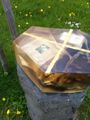 Auf einem Steinpodest sind bedeutsame Gegenstände sowie ein Zeitungsartikel in Harz gegossen für Besucher als Gedenkstein aufgestellt worden.