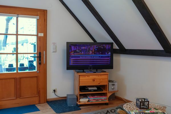 Fernseher auf kleinem Holzschrank neben einer Tür mit Glasfenster unter Dachschräge