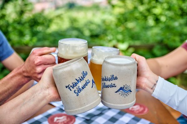 Bierkrüge mit der Aufschrift Fränkische Schweiz werden hochgehoben und stoßen miteinander an.