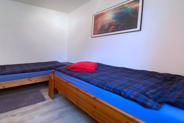 Zwei Einzelbetten mit dunkler Bettwäsche und rotem Handtuch in einem Schlafzimmer