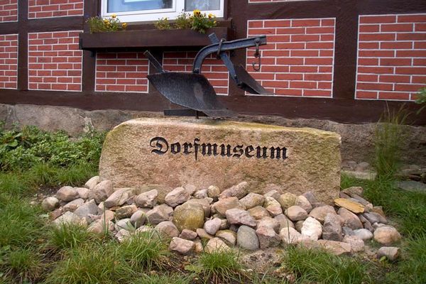 Stein mit Aufschrift "Dorfmuseum" und ein kleiner alter Pflug oben auf