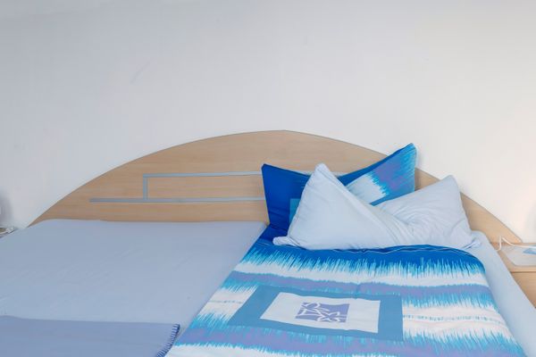 Bett mit blauer gemusterter Bettwäsche und Kissen, flankiert von zwei Nachttischen mit Lampen