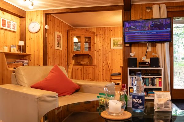 Wohnzimmer mit Sofa, Couchtisch und Fernseher an der Wand, daneben Regal und Tür.