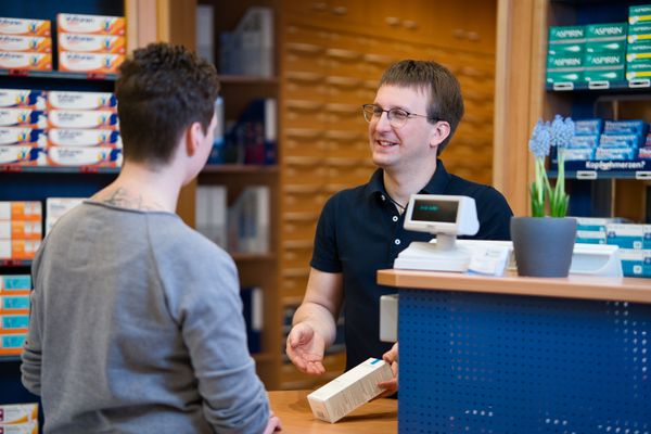 Auf dem Bild ist ein Kundengespräch zwischen einer Kundin und dem Apotheker an der Kasse zu sehen.