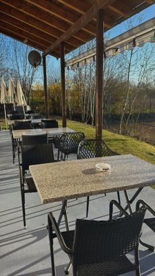 Auf dem Foto sieht man die Terrasse der Pizzeria mit Tischen und Stühlen und einer Überdachung der Terrasse im Sonnenuntergang.