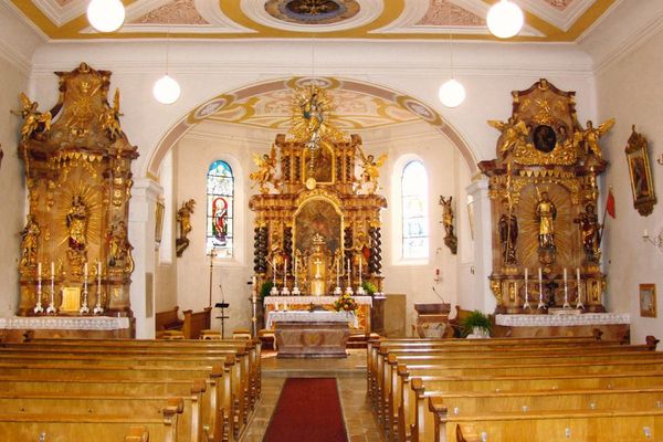 Der Innenraum der Pfarrkirche St. Jakob ist von goldenen Elementen geprägt. Zu sehen sind ein Hauptaltar und zwei Nebenaltäre, umgeben von kunstvollen Verzierungen und Dekorationen.