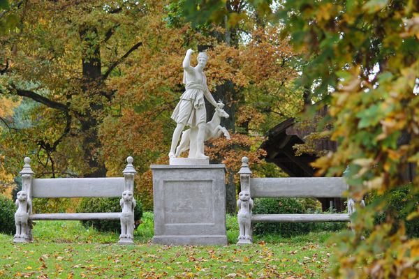Ein steinernes Monument mit beidseitig davon stehenden steinernen Parkbänken befinden sich inmitten eines Parks.