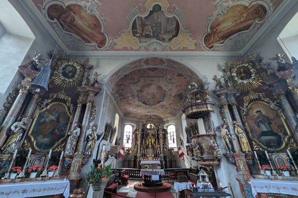 Das Bild zeigt den Innenraum der Wallfahrtskirche Mariä Geburt in Glosberg. Man sieht Sitzbänke und prunkvolle Altäre, Gemälde und Statuen.