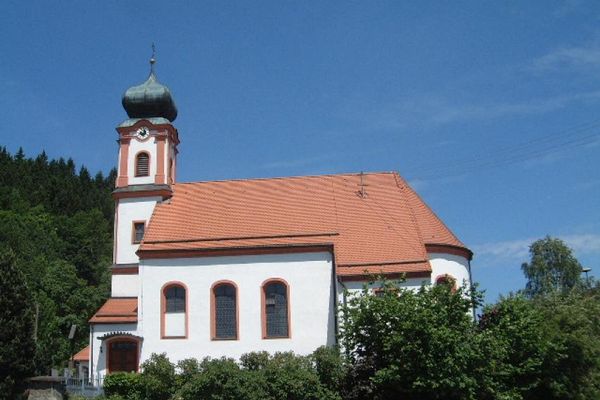 Auf einem Hügel, umgeben von Bäumen und Sträuchern, steht die Pfarrkirche St. Laurentius mit viereckigem Turm und Zwiebelkuppel.