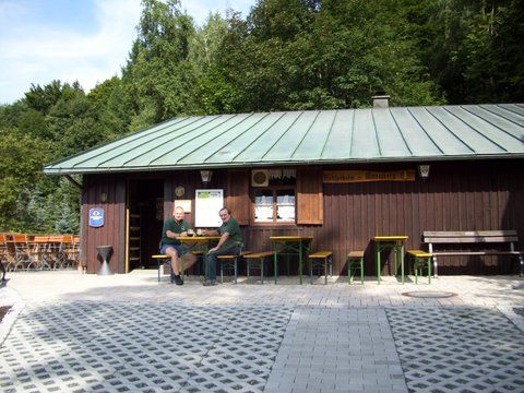 Das Bild zeigt die Radspitzalm sowie die Terrasse davor, es sind Biertischgarnituren zu sehen sowie zwei Wanderer, die Pause machen.
