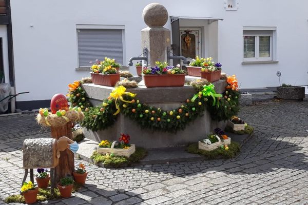 Um den runden Steinbrunnen hängen Girlanden aus Nadelzweigen, die mit bunten Eiern und Schleifen verziert sind.