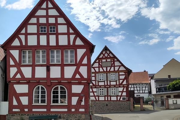 Fachwerkhäuser mit rotem Gebälk, weißen Gefachen und Sockeln aus Sammelsteinen sind hintereinander versetzt zu sehen. Die gepflegten Häuser wirken einladend an diesem sonnigen Tag.