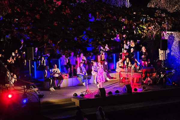 Bunt beleuchtete Bühne mit Musikern, Pianospiele und Publikum im Hintergrund