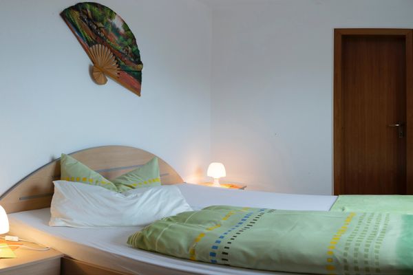 Einzelbett mit grüner Bettwäsche und zwei Nachttischen mit Lampen, daneben eine Tür