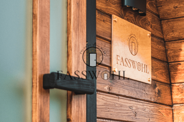 Auf dem Bild ist die Tür der Fass-Sauna mit Schild "FASSWOHL" zu sehen.