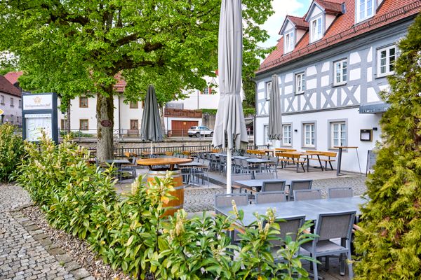 Blick durch Büsche auf ein grau-weißes Fachwerkhaus.