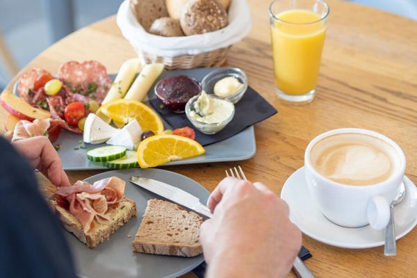 Frühstücksplatte, Brötchen, Kaffee, Orangensaft, eine Person macht sich ein Schinkenbrot
