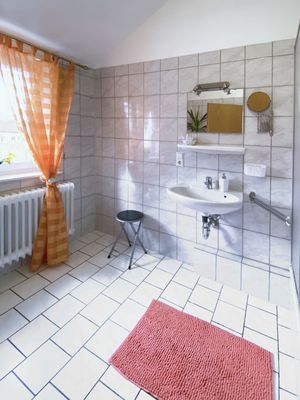 Bad mit Waschbecken, Spiegel, Fenster mit Vorhang, Hocker und Teppich auf gefliestem Boden