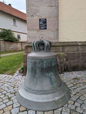 Auf dem Bild sieht man eine Kircheglocke im Hof der Wallfahrtskirche Mariä Geburt in Glosberg.