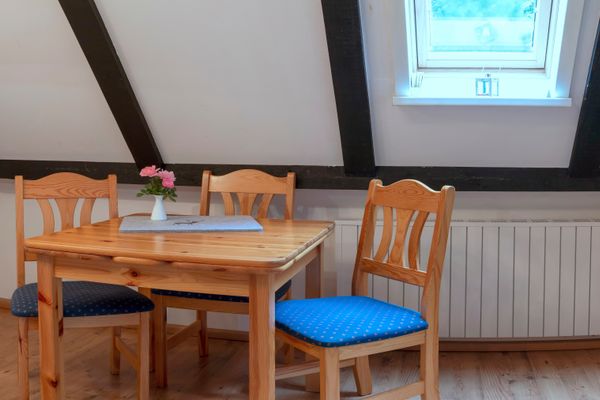 Holztisch mit drei Stühlen unter Dachschräge, Fenster und sichtbare Deckenbalken