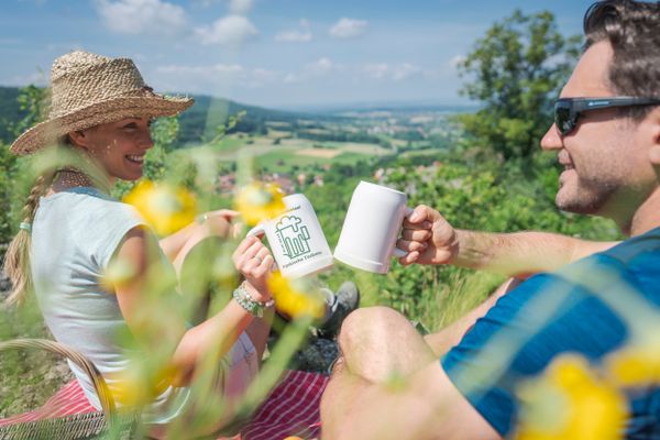 Pärchen auf einem Aussichtspunkt, sitzend mit einen Bierkrug in der Hand und Blick ins Ellertal.