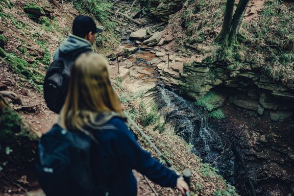 Zwei Wanderer stehen oberhalb der Margaretenschlucht und blicken hinab in die Schlucht, durch die ein Wasserfall fließt.