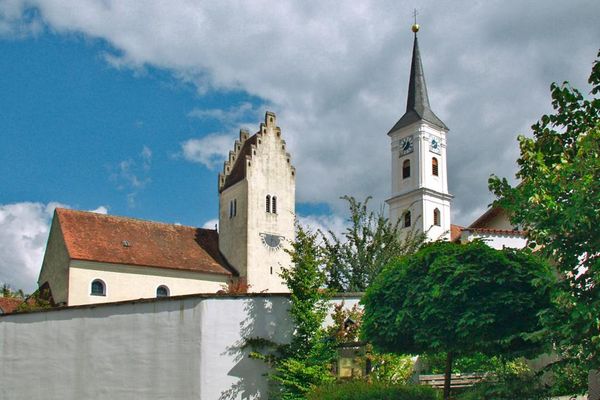 Hinter einer hohen Mauer steht die Kirche St. Tiburtius in Münster mit zwei Türmen: einer mit Treppengiebel-Dach, der andere viereckig mit Spitzdach und Doppelkreuz. Vor der Mauer stehen Bäume und eine Bank.