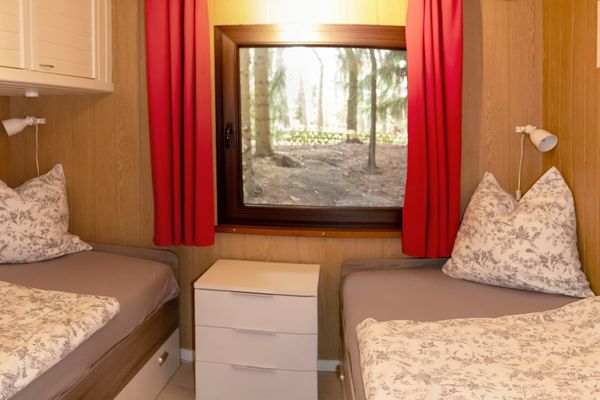 Zweibettzimmer mit zwei Einzelbetten, Nachttisch und Fenster mit roten Vorhängen.