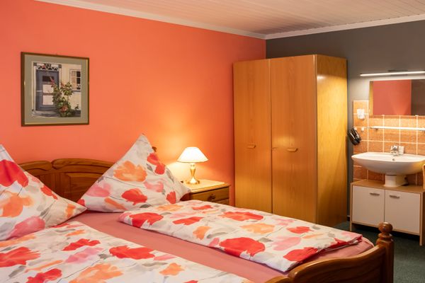 Schlafzimmer mit Doppelbett, Kleiderschrank und Waschbecken mit Spiegel, beleuchtet durch Tischlampe.