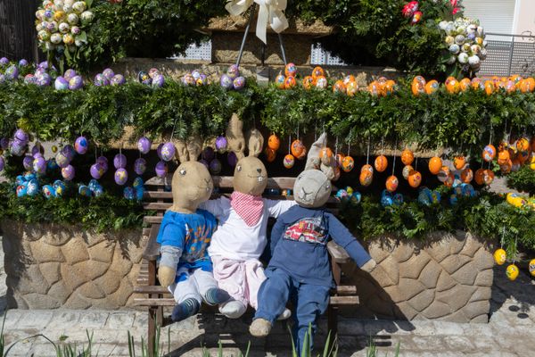 Drei bekleidete Hasen aus Sackleinen, die auf einer Bank für dem Osterbrunnen sitzen.