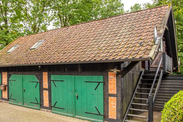 Gebäude mit Ziegeldach, mehreren grünen Toren und seitlicher Außentreppe aus Holz