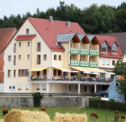 Landhotel mit umlaufender Terrasse, im Vordergrund Kühe auf der Weide