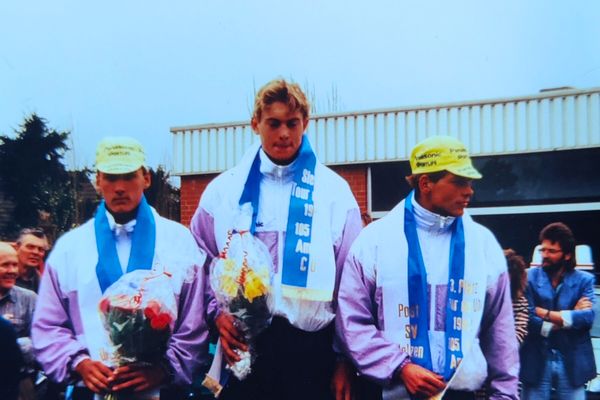 Siegerehrung beim Straßenradrennen „Tour de Uhl“ im Jahr 1992. Die Radfahrer André Korff, Ralf Grabsch und Jan Ullrich stehen nebeneinander auf dem Podium. Sie tragen Sportbekleidung und Siegerbänder und halten Blumensträuße. Im Hintergrund sind Zuschauerinnen und Zuschauer sowie Gebäude zu sehen.