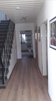 Im Flur führt links eine Treppe in den ersten Stock. Gegenüber befinden sich zwei Türen, dazwischen hängen Bilder an der Wand.