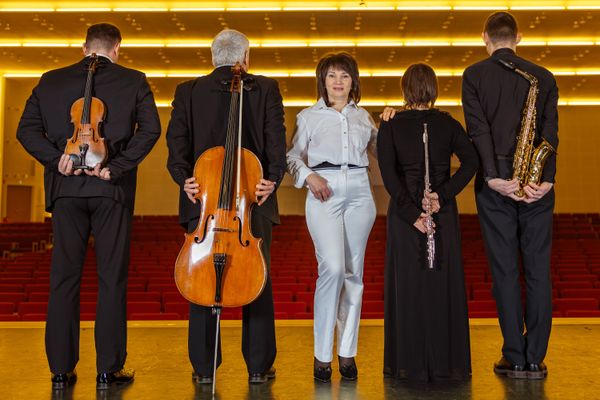 Die Ensemble-Leiterin in weiß in der Mitte mit Blick nach vorne und vier schwarz gekleidete Musiker mit ihren Instrumenten vor dem Rücken neben sich